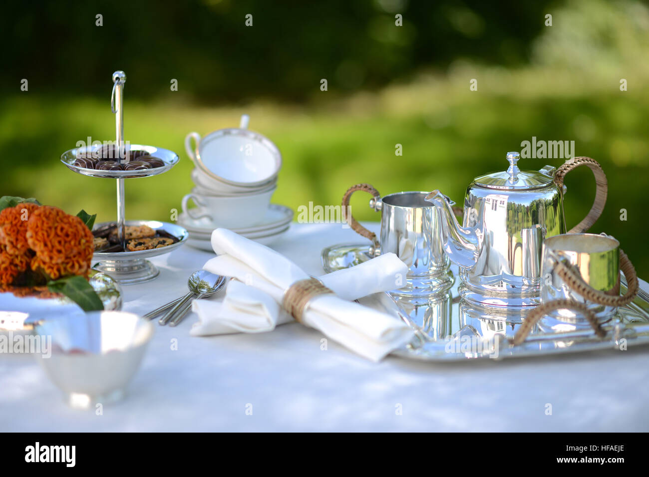 Table set for an English high tea, or afternoon tea, outside with silver teapot and linen tablecloth Stock Photo