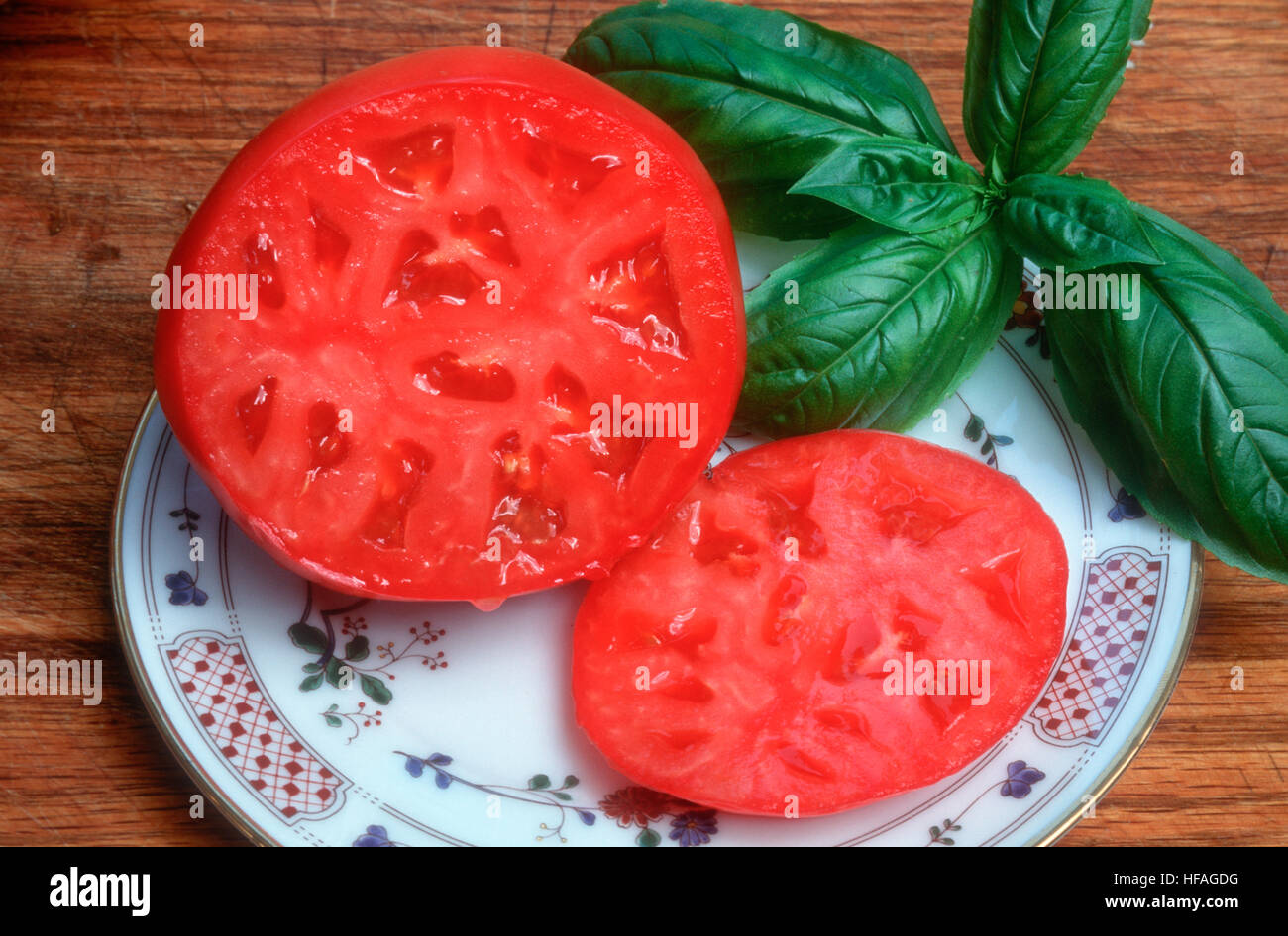 Tomato sliced open on plate with basil herb, seedless beefsteak vegetable freshly cut ripe red just picked ready to eat healthy Stock Photo