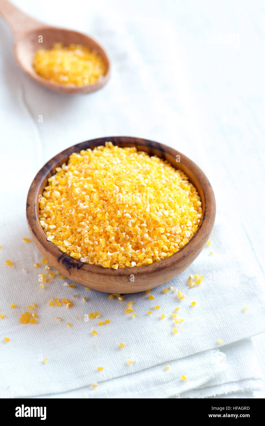 Raw organic Polenta Corn Meal (Grits) in wooden bowl over white