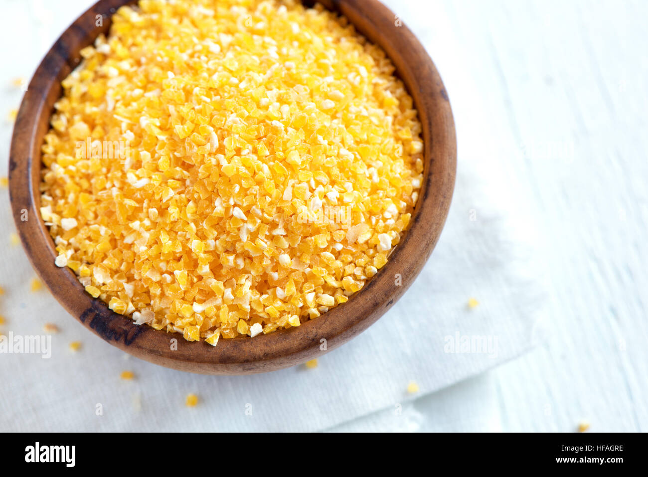 Raw organic Polenta Corn Meal (Grits) in wooden bowl over white