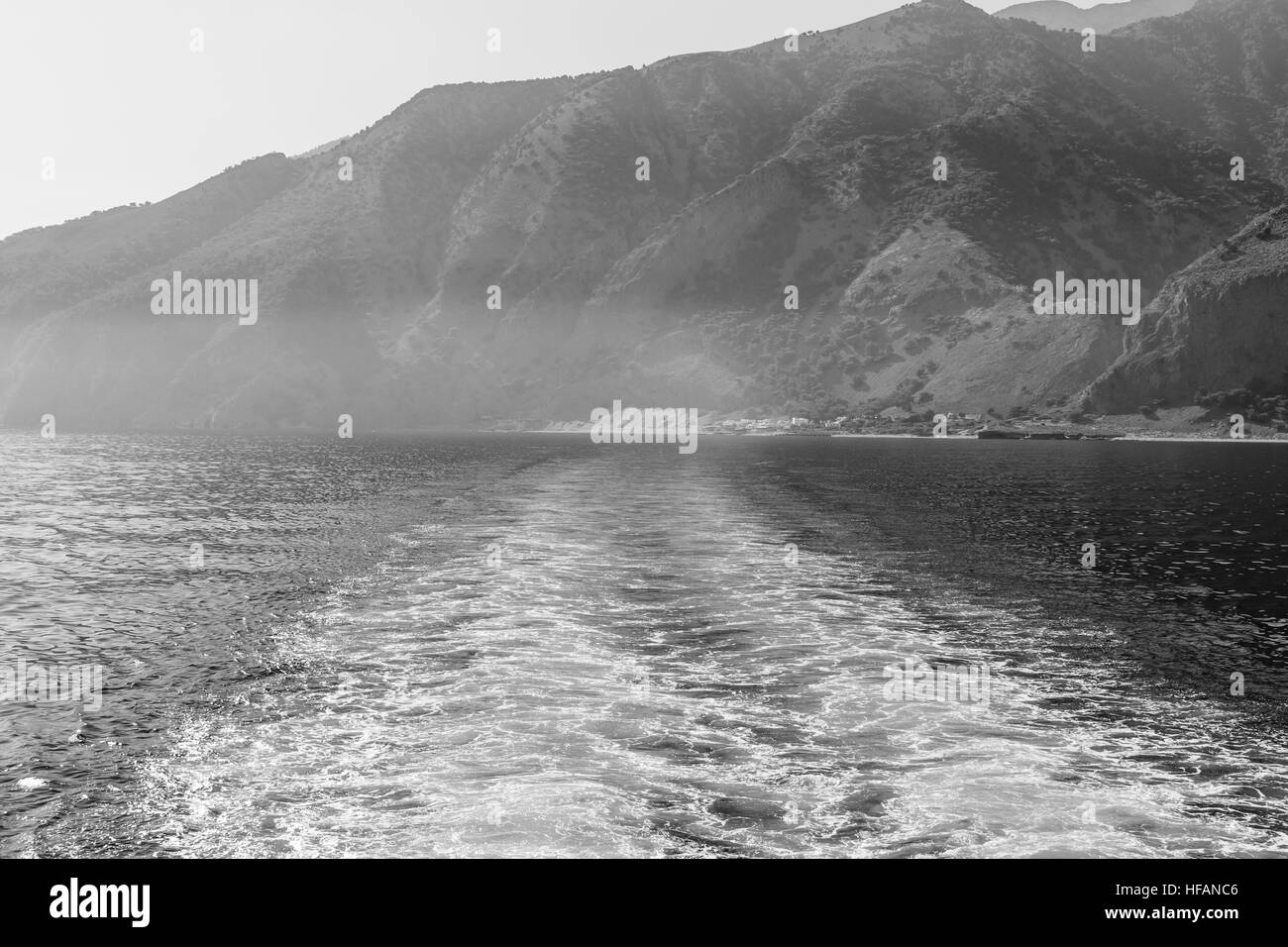 Mountains of southern coast of Crete. Waves (traces of movement) of the ship going in the distance. Black and white. Stock Photo