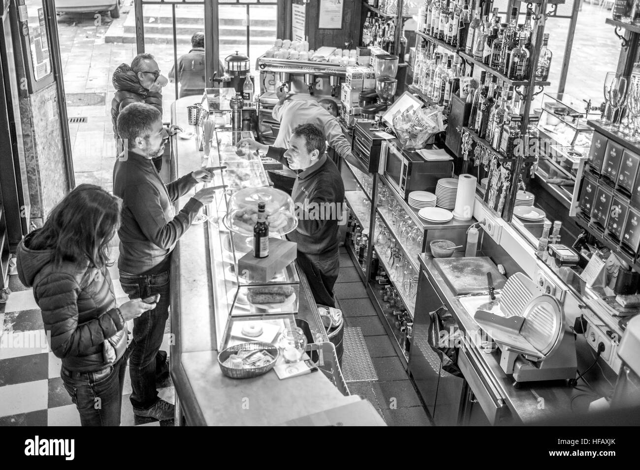 A tapas cafe in Barcelona is bustling and busy in the morning as a man orders jamon croissant hot chocolate from a Catalan man Stock Photo