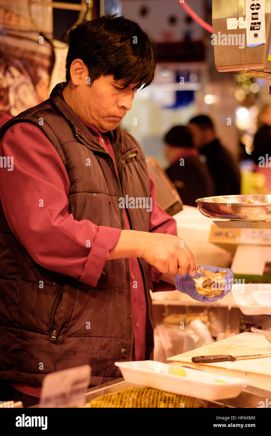 A spanish man serves fresh oysters ready to eat from a stall in an outdoor market in Barcelona Stock Photo