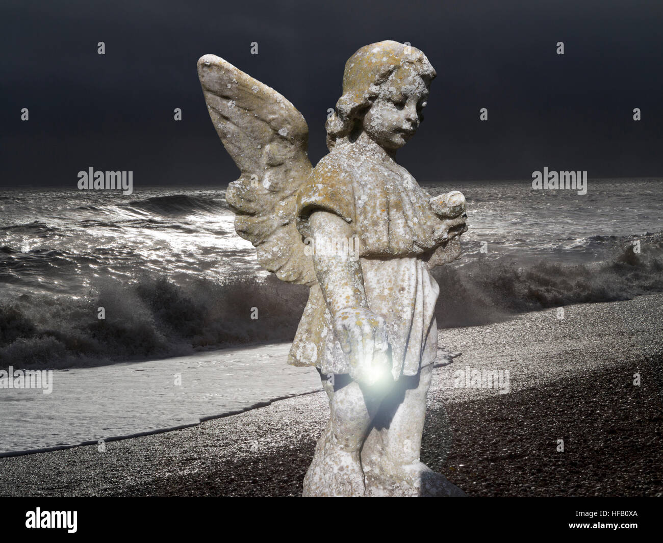 A dramatic image of a tombstone angel on a moonlit beach with heavy breaking waves on the shoreline Stock Photo