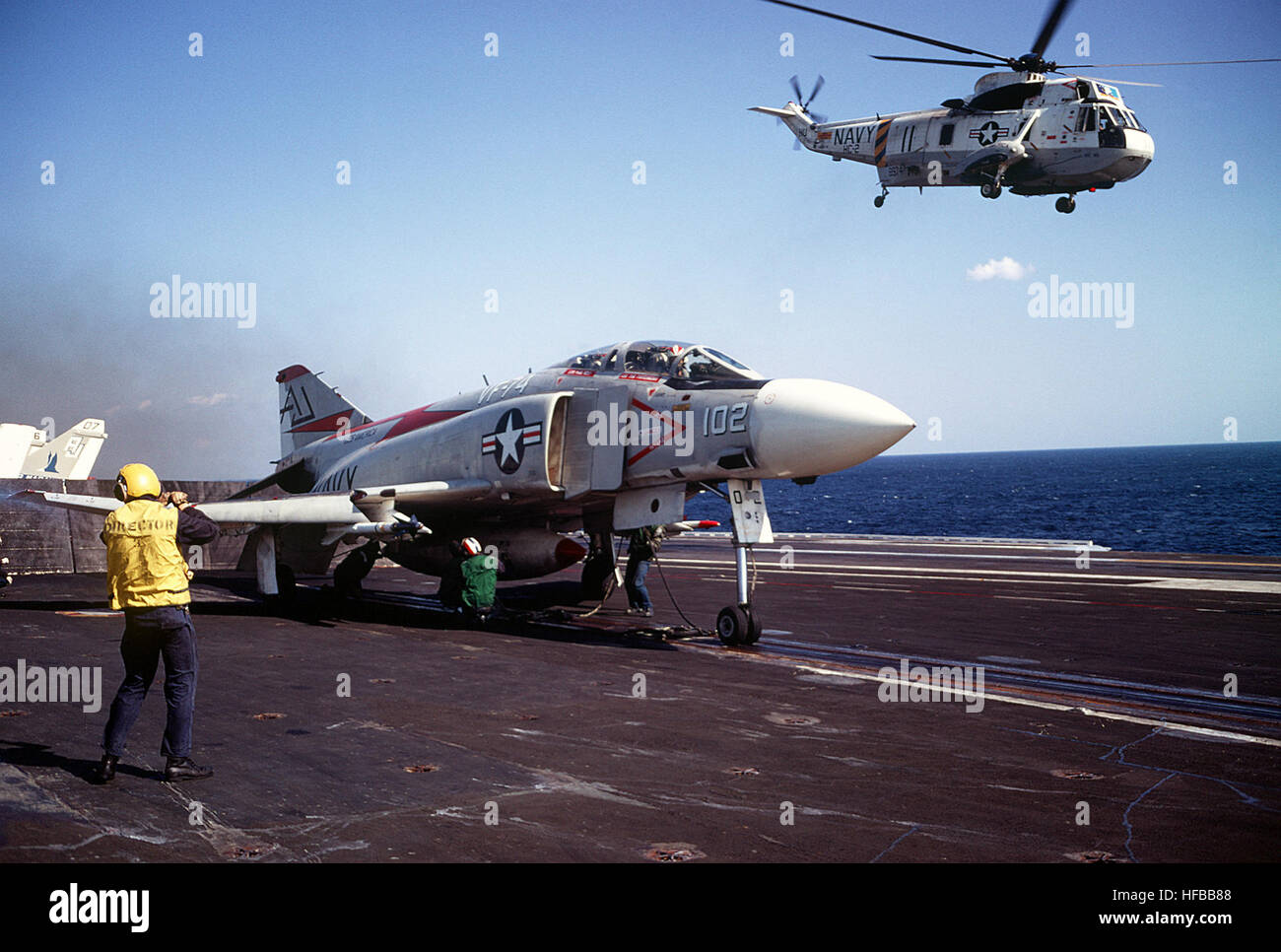 A plane director stands by as other flight deck crewmen prepare a
