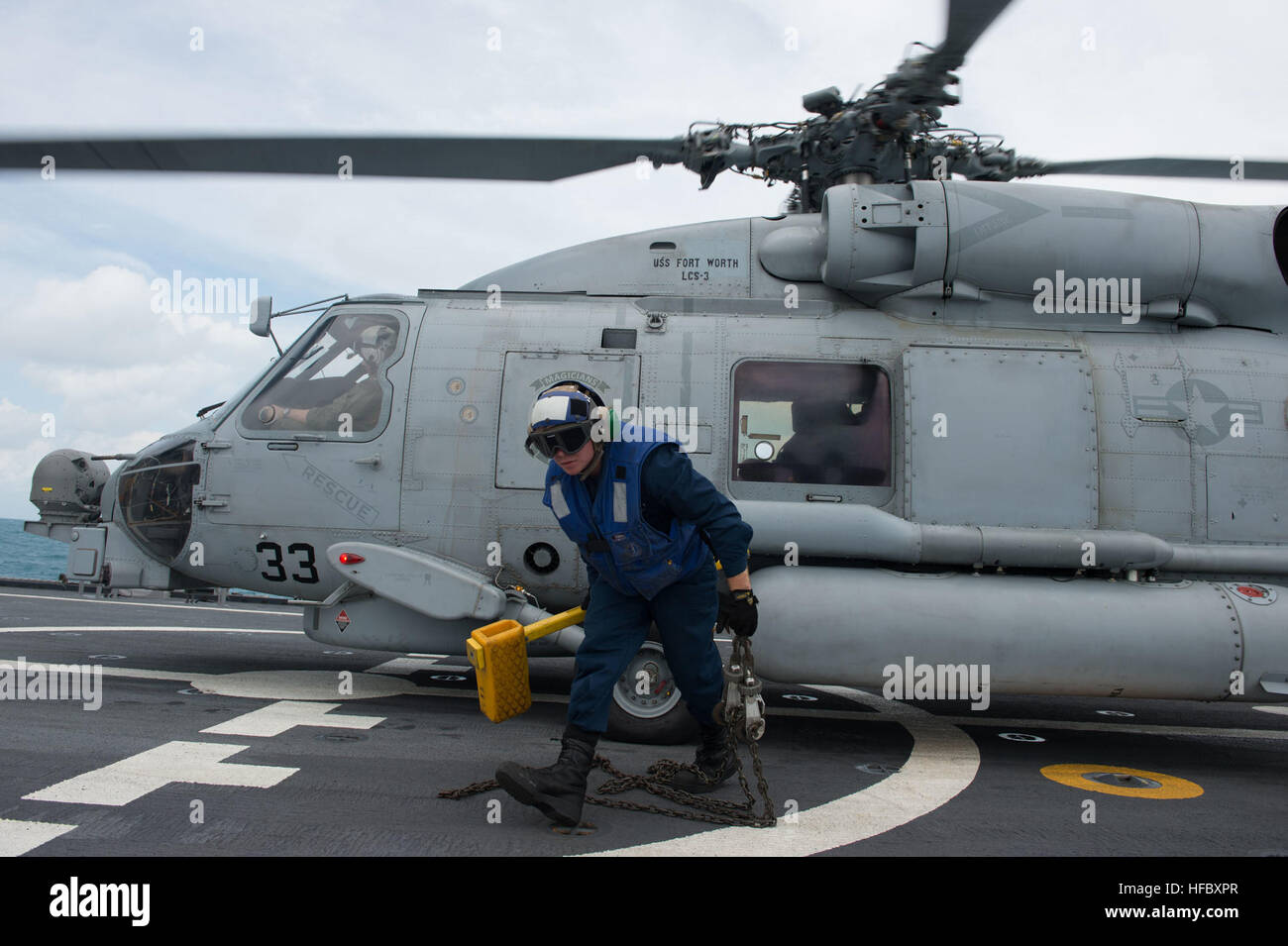 Boatswains Mate 2nd Class James Fitzpatrick removes the chocks and chains on a MH-60R Seahawk helicopter from Helicopter Maritime Strike Squadron 35 on board the littoral combat ship USS Fort Worth (LCS 3). Fort Worth is supporting Indonesian-led search efforts to locate AirAsia Flight QZ8501 and is operating in the vicinity of where the plane’s tail was discovered. (U.S. Navy photo by Mass Communication Specialist 2nd Class Antonio P. Turretto Ramos/Released) Flight operations aboard USS Fort Worth (LCS 3) 150110-N-DC018-130 Stock Photo