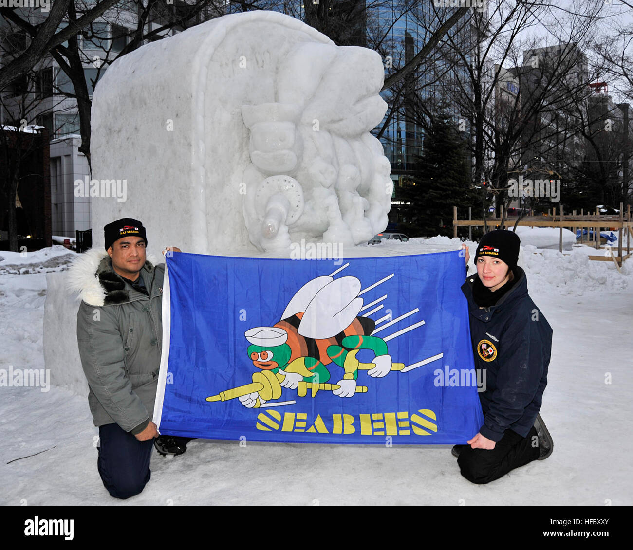 Chief Builder Billy Harger, left, originally from Pearl City, Hawaii, and Utilitiesman Constructionman Ariel Hogue, a native of Pensacola, Fla., display a flag emblazoned with the U.S. Navy Seabee's 'Fighting Bee' design, Feb. 3, 3014.  Both sailors are attached to Naval Facilities Engineering Command Far East Detachment Misawa, and are also members of the 2014 Navy Misawa Snow Team, which is in Hokkaido, Japan, taking part in the 65th Annual Sapporo Snow Festival.  The team sculpted a frosty, 3-D version of the U.S. Navy Seabee's 'Fighting Bee' logo.  This is the 31st year that Naval Air Faci Stock Photo