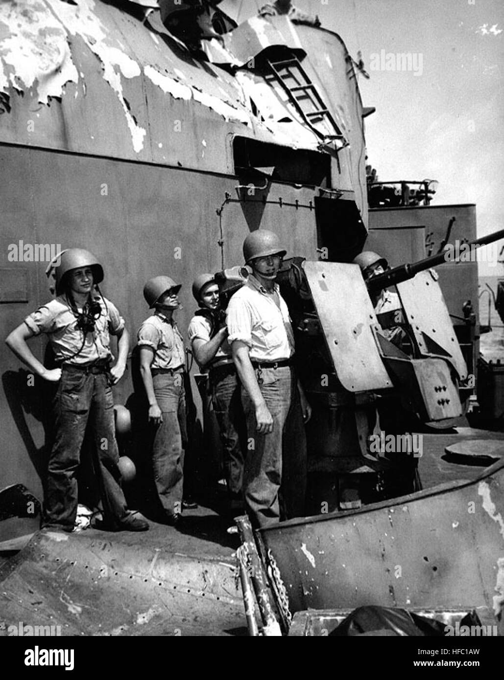 Crew of one of the ship's port forward 20mm guns pose by their weapon, at Guam, circa 16 June 1945. They had stuck to their post until knocked off their feet by the force of a second explosion, when Lindsey was struck by two Kamikaze planes off Okinawa on 12 April 1945. Note severely damaged plating in the vicinity. The men are (left to right): CM3c Edwin K. Kayden; GM3c Balanor Easebio; Y2c Chester F. Fluharty; S1c Fred M. Gorges; S1c Robert F. Zelenka.  Official U.S. Navy Photograph, now in the collections of the National Archives. Gun crew on USS Lindsey (DM-32) in June 1945 Stock Photo