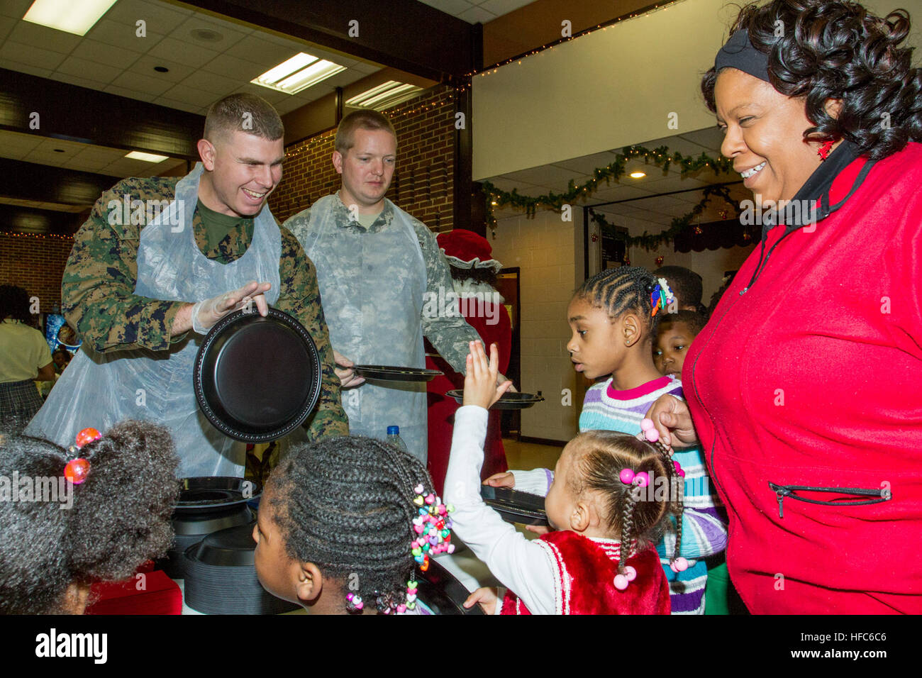 Marine Sgt. Ryan Stitzel, of Fleetwood, Pa., assigned to the Marine Barracks Washington exchanges smiles with a child as he serves her up a delicious warm lunch. Military and civilian personnel and their families, living or working at Joint Base Anacostia-Bolling (JBAB) volunteered and helped make the Christmas holiday season more joyful for nearly 300 youth in the District of Columbia's Ward 8 at a Disadvantaged Youth Holiday Party, sponsored by the Metropolitan Police Department's Seventh District on Dec. 18. The JBAB volunteers helped serve food to the children, pass out gifts and help with Stock Photo
