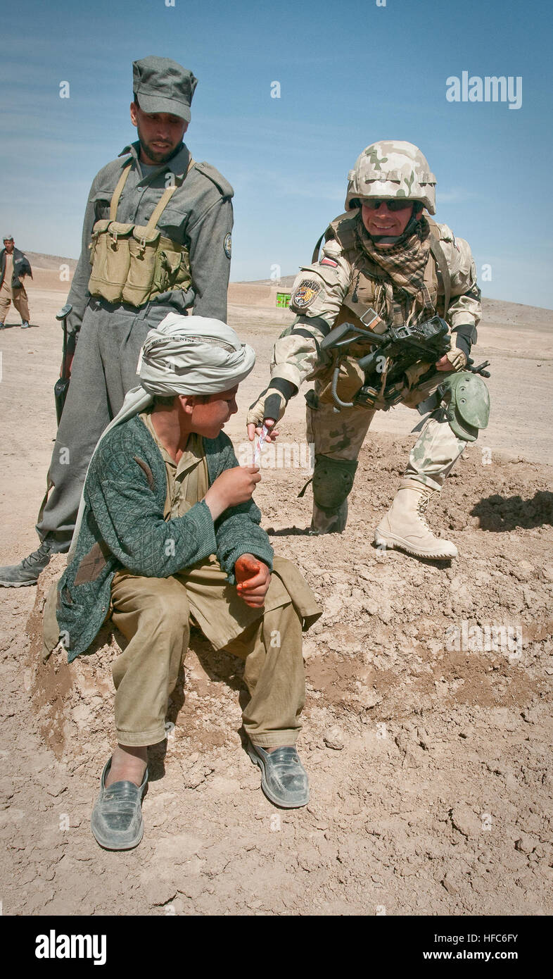 GHAZNI PROVINCE, Afghanistan (March 17, 2010) – A Polish Army soldier extends an offering to a local boy in the Giro District of Ghazni Province as an Afghan policeman looks on. (U.S. Navy photo by Petty Officer 1st Class Mark O’Donald/Released) Joint Patrol in Ghazni Province 274031 Stock Photo