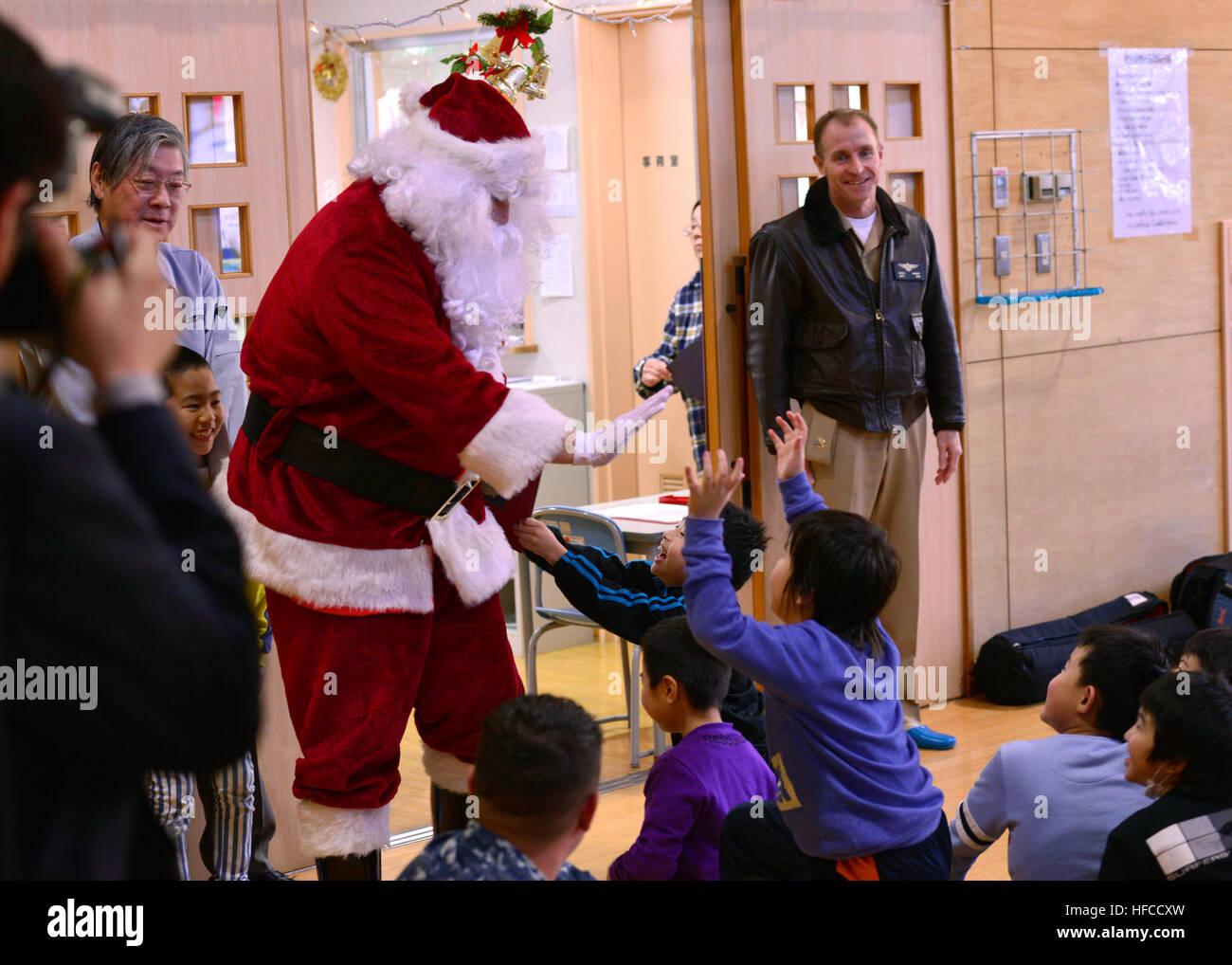 161219-N-OK605-020 MISAWA, Japan (Dec. 19, 2016) Capt. Keith Henry, commanding officer Naval Air Facility Misawa (NAFM), looks on as Petty Officer 1st Class Donald McDowell, attached to NAFM, high-fives children on his arrival to the Ohzora Jido-Kan, a Japanese after school care center, as Santa Claus for a special holiday themed visit. Sailors from NAFM volunteer to make bi-weekly visits to the after school care center as part of community relations efforts. (U.S. Navy Photo by Petty Officer 2nd Class Samuel Weldin/Released) Misawa Sailors Visit Japanese After School Program for the Holidays  Stock Photo