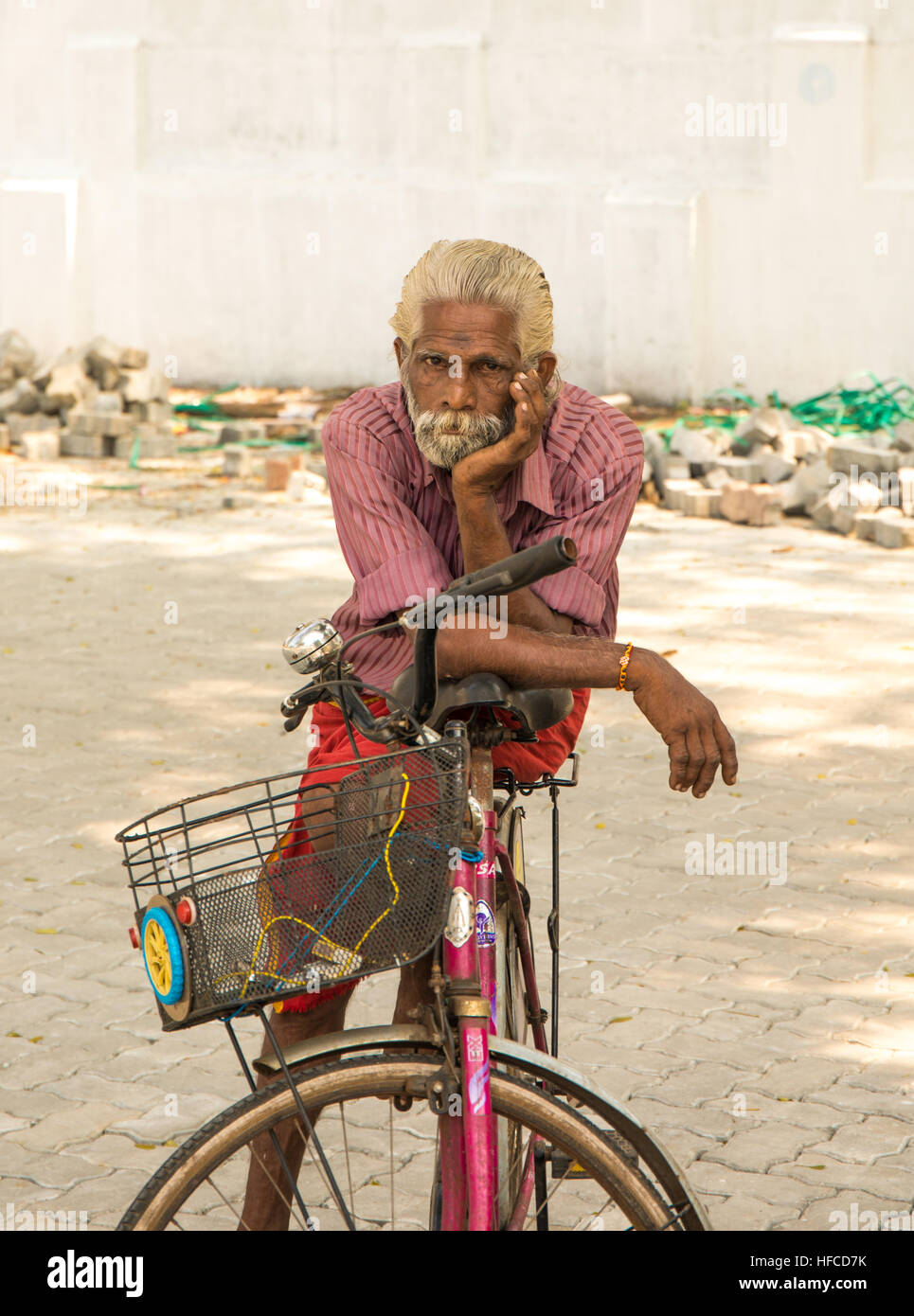 Old Indian man with grey hair and a grey bear sitting on his bicycle Stock Photo