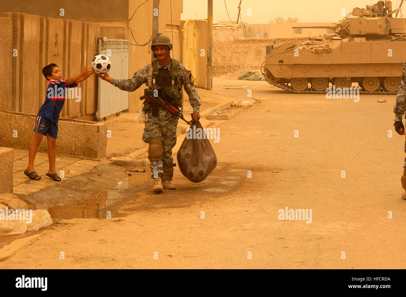 An Iraqi boy reaches out to receive a soccer ball from a policeman. Iraqi national police and U.S. Soldiers from 64th Armored Calvary Regiment, 4th Brigade, 3rd Infantry Division searched a mullalah in Risalah, Baghdad on Sep. 15, 2008, in order to document the local military aged males residing there. Police, Soldiers Visit Iraqi Civilians 116057 Stock Photo