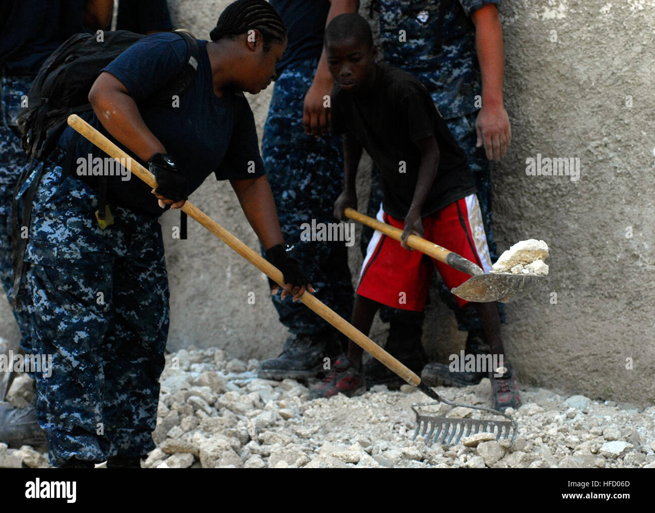A Haitian boy helps Petty Officer 2nd Class Shaunte Stafford, an information systems technician assigned to Amphibious Construction Battalion 2, remove rubble from his former school. Amphibious Construction Battalion 2 is conducting humanitarian and disaster relief operations as part of Operation Unified Response after a 7.0 magnitude earthquake caused severe damage in and around Port-au-Prince, Haiti, Jan. 12. Sailors assist in Haiti 252961 Stock Photo