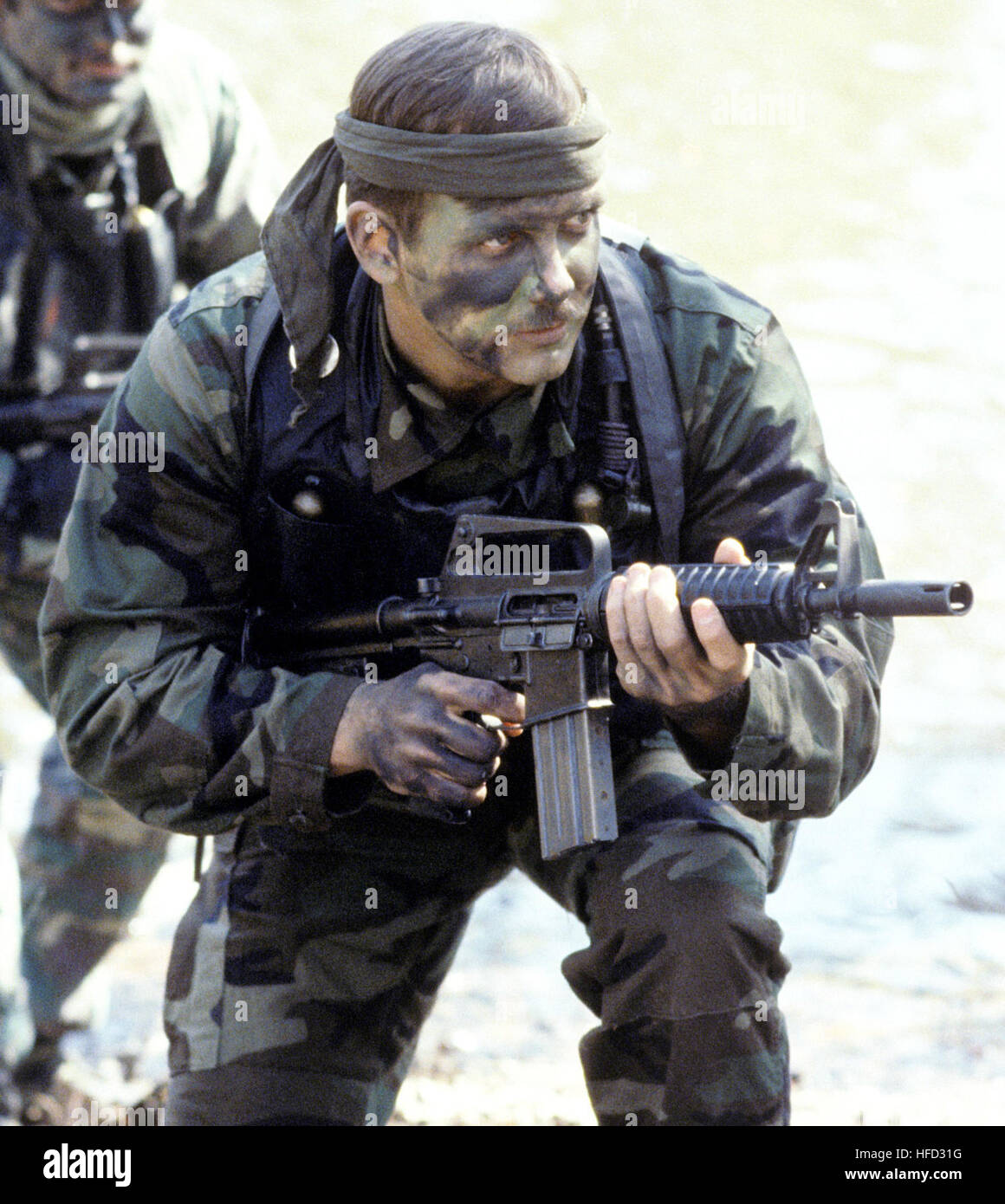 Boatswain's Mate 1st Class Mark Blasen, foreground, and Photographer's Mate 2nd Class Peter Rogers, both members of Sea-Air-Land (SEAL) Team 4, participate in a training exercise.  Blasen is armed with a 5.56 mm Colt Commando assault rifle/submarine gun.  All Hands - April 1985. SEAL Colt Commando v2 Stock Photo