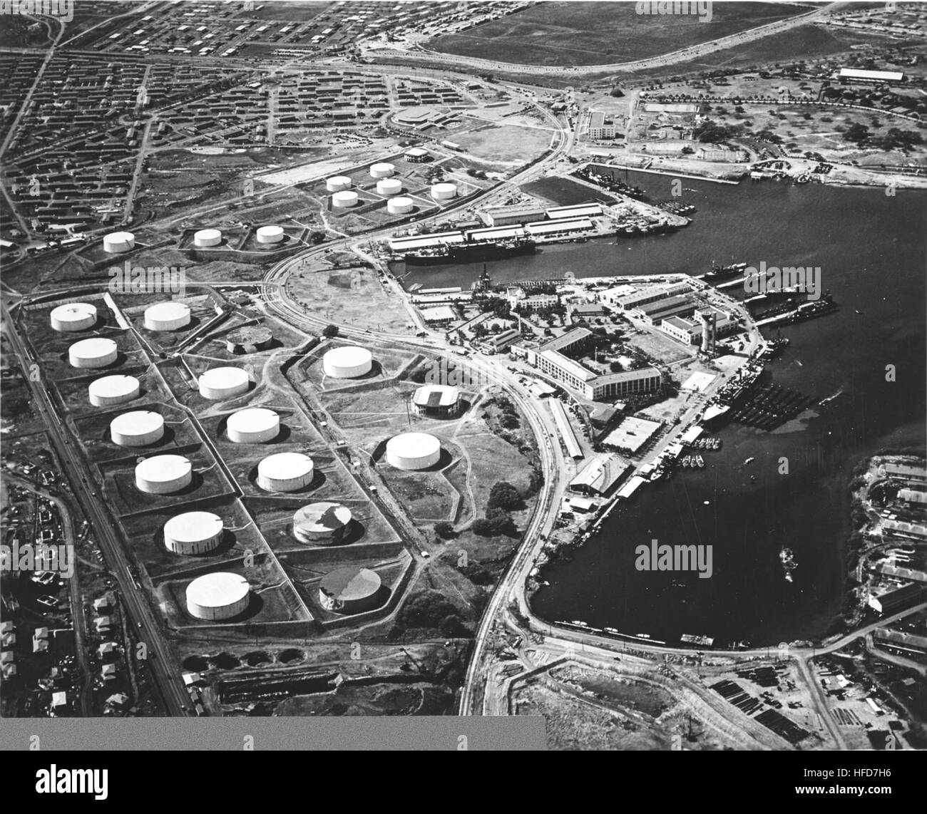 Aerial view of the Submarine Base (right center) with the fuel farm at left, looking south on 13 October 1941. Among the 16 fuel tanks in the lower group and ten tanks in the upper group are two that have been painted to resemble buildings (topmost tank in upper group, and rightmost tank in lower group). Other tanks appear to be painted to look like terrain features. Alongside the wharf in right center are USS Niagara (PG-52) with seven or eight PT boats alongside (nearest to camera), and USS Holland (AS-3) with seven submarines alongside. About six more submarines are at the piers at the head Stock Photo