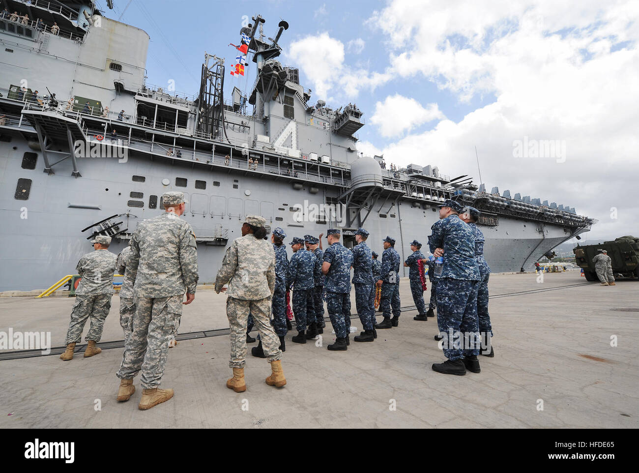 U.S. Service members greet the amphibious assault ship USS Boxer (LHD 4) as the ship arrives at Joint Base Pearl Harbor-Hickam, Hawaii, April 15, 2014. The Boxer conducted a deployment in the U.S. 5th Fleet and 7th Fleet areas of responsibility and participated in Ssang Yong 14 during Marine Expeditionary Force Exercise (MEFEX) 2014. MEFEX 2014 was a U.S. Marine Corps Forces Pacific-sponsored series of exercises between the U.S. Navy and Marine Corps and South Korean forces. Among the exercises were the Korean Marine Exchange Program, Freedom Banner 14, Ssang Yong 14, Key Resolve 14 and the Co Stock Photo