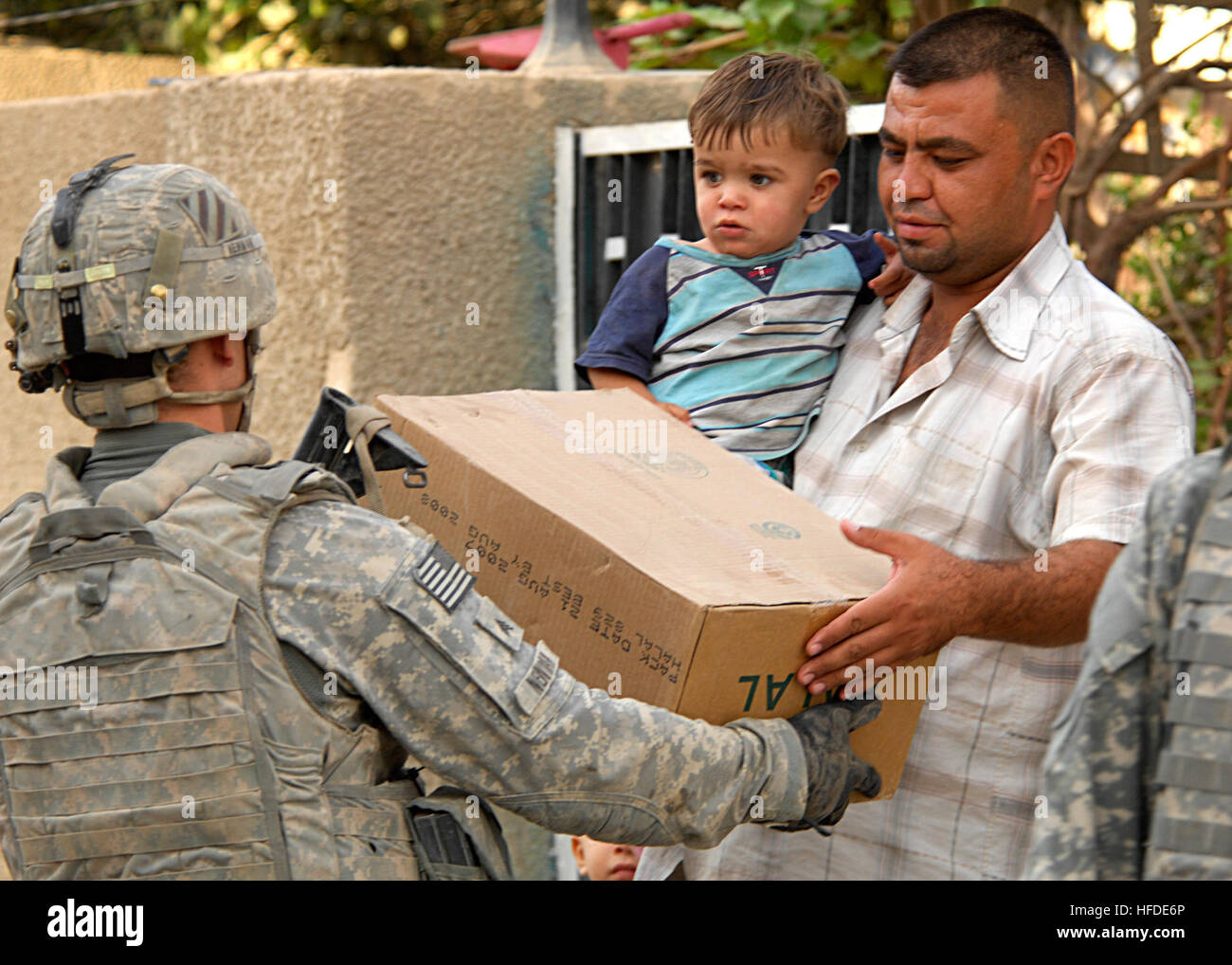 A U.S. Soldier gives a box of Halal food to an Iraqi man and his child. Iraqi national police and U.S. Soldiers from 3rd Infantry Division, 4th Brigade, 64th Cavalry searched for weapons cache in Risalah, Baghdad on Sept. 26, 2008. U.S. Soldiers, Working Dogs Search for Weapons Cache 118646 Stock Photo