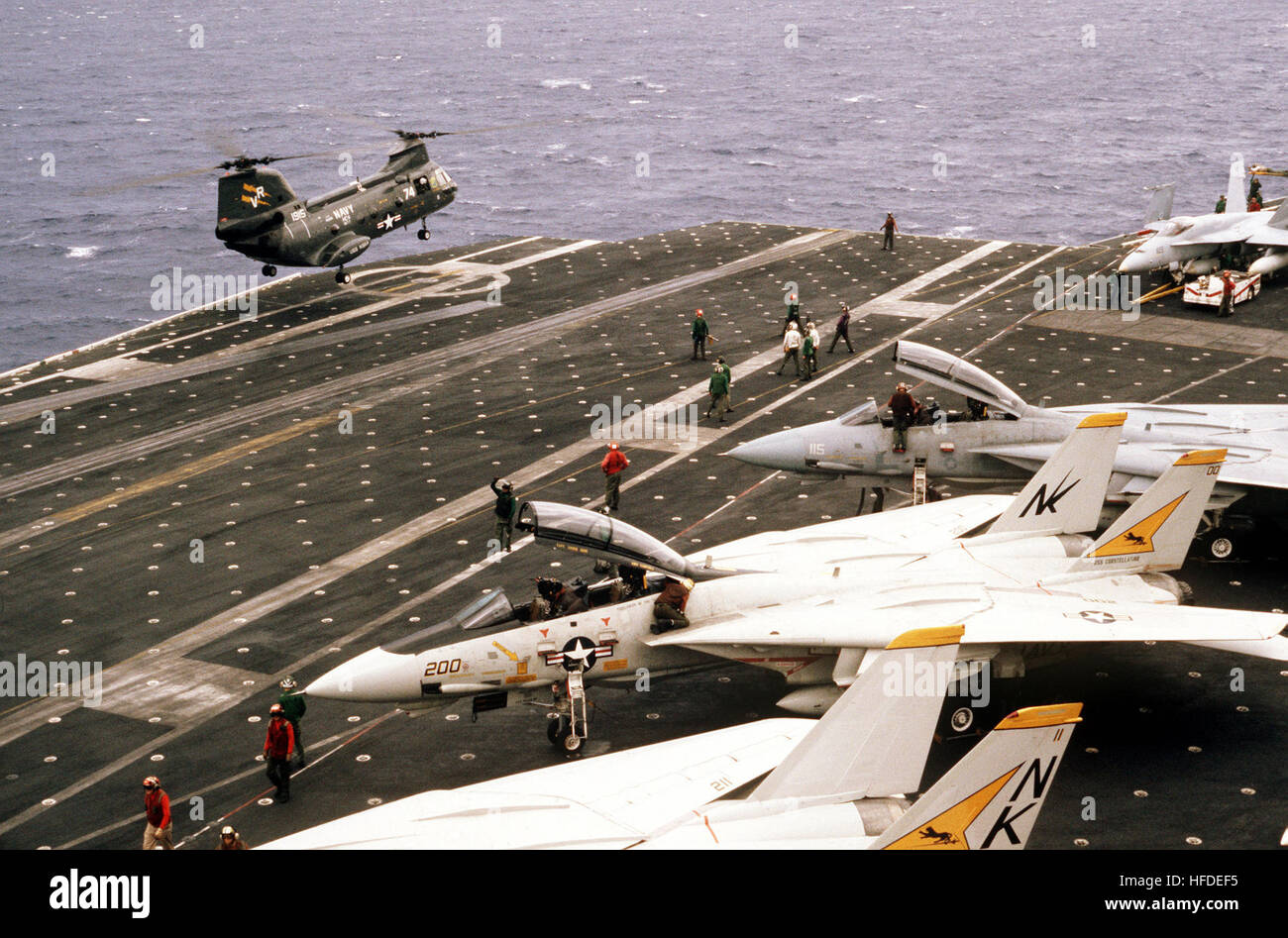 A UH-46D Sea Knight helicopter from the ammunition ship USS KISKA (AE 35) hovers above the flight deck of the aircraft carrier USS CONSTELLATION (CV 64) during Fleet Exercise 85.  In the foreground are several F-14A Tomcat aircraft from Fighter Squadron 21.  On the far right is an F/A-18A Hornet aircraft. UH-46D landing on USS Constellation (CV-64) 1984 Stock Photo