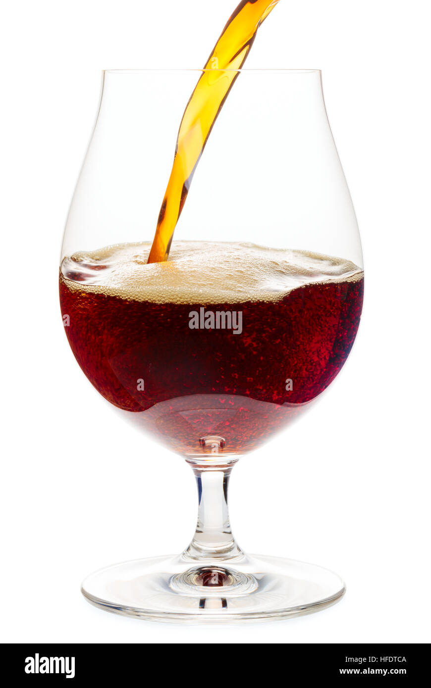 Dark ale or porter beer is pouring into snifter glass isolated on white