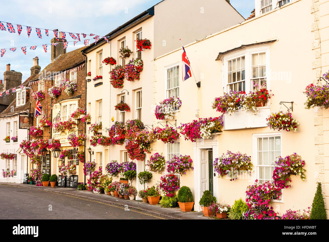 England, Deal. View along row of 17th and 18th century buildings along seafront, all decked with red flowers in boxes. Picturesque. Sunlit. Union Jack. Stock Photo