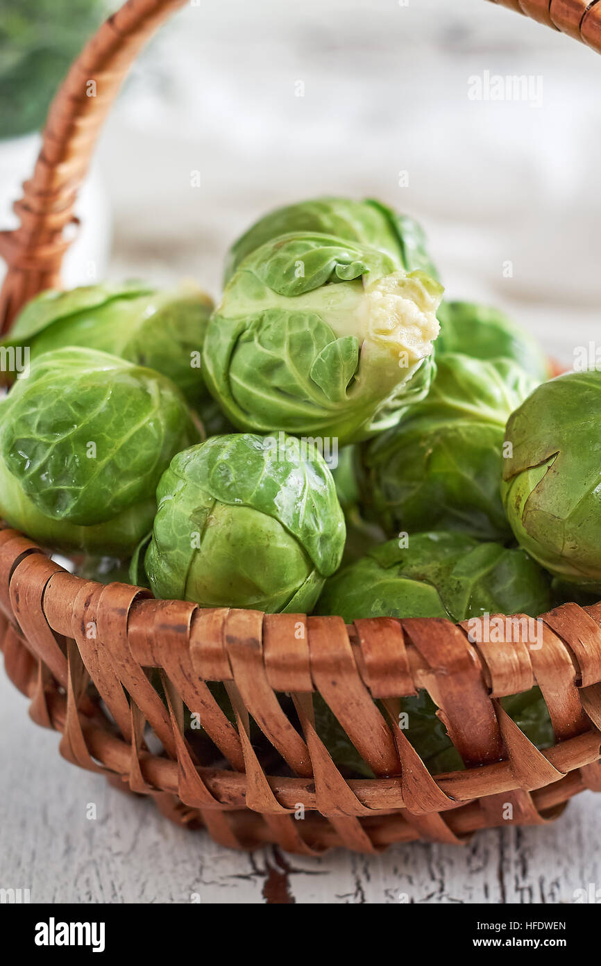 Fresh raw brussel sprouts in woven basket on white rustic wooden background Stock Photo
