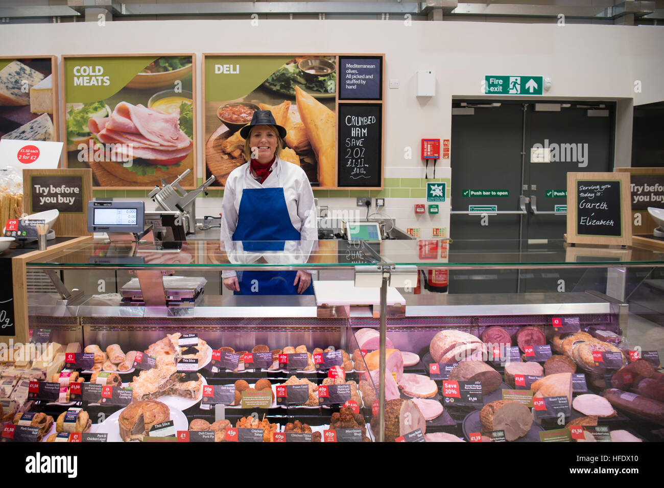 A woman working behind a fresh cooked meat goods food counter in Tesco