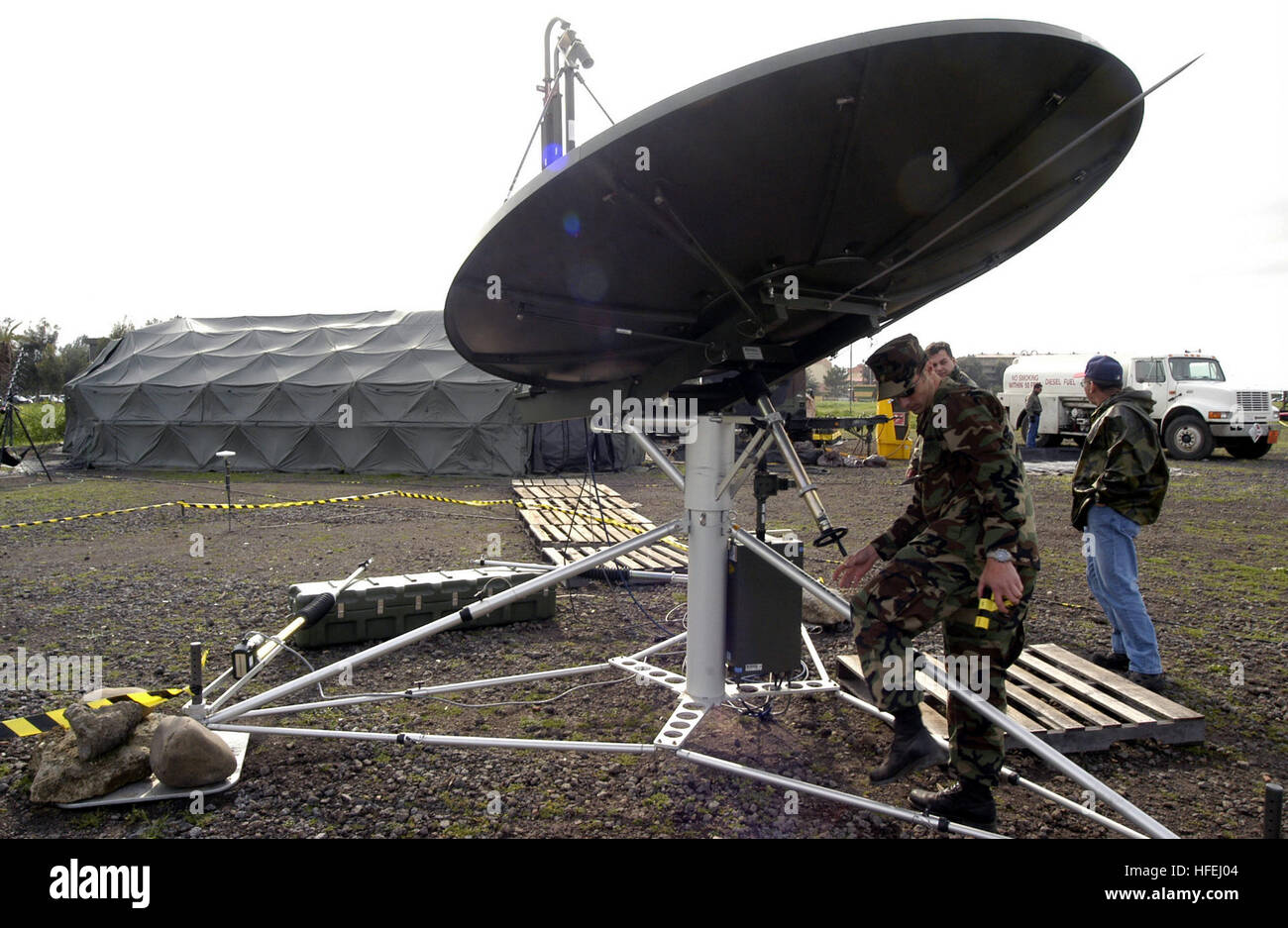 030403-N-9693M-004 Naval Air Station Sigonella, Sicily (Apr. 3, 2003) -- Electronics Technician 2nd Class Kristian Dillemouth stows a USC-60A satellite dish for the evening as part of a systems operability test of the Joint Mobile Ashore Support Terminal (JMAST) Europe.  Three deployable rapid assembly shelters (DRASH) in the background serve as the operations, briefing, and communications centers for JMAST Europe when deployed.  JMAST is a self-contained mobile command, control, communications, computer, and intelligence (C4I) center designed to support the Naval component commander in joint  Stock Photo