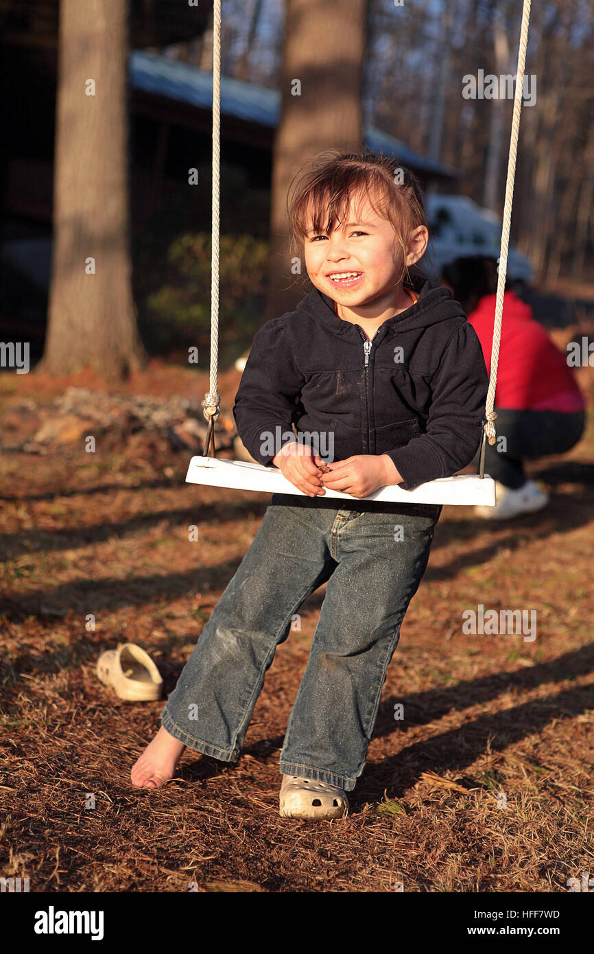 A cute three-year old girl wearing one shoe plays on a swing in her backyard Stock Photo