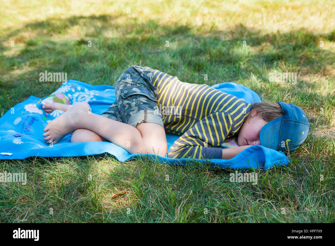 Child sleeping on a blue blanket on grassy ground at a campground in Vermont, USA. Stock Photo