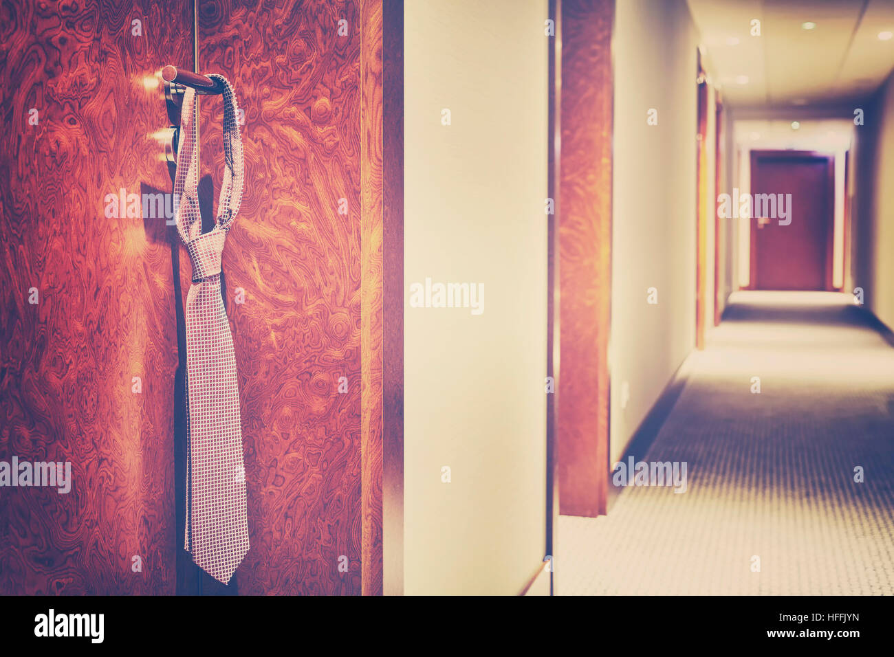Vintage stylized tie hanging on a hotel closed door handle. Stock Photo