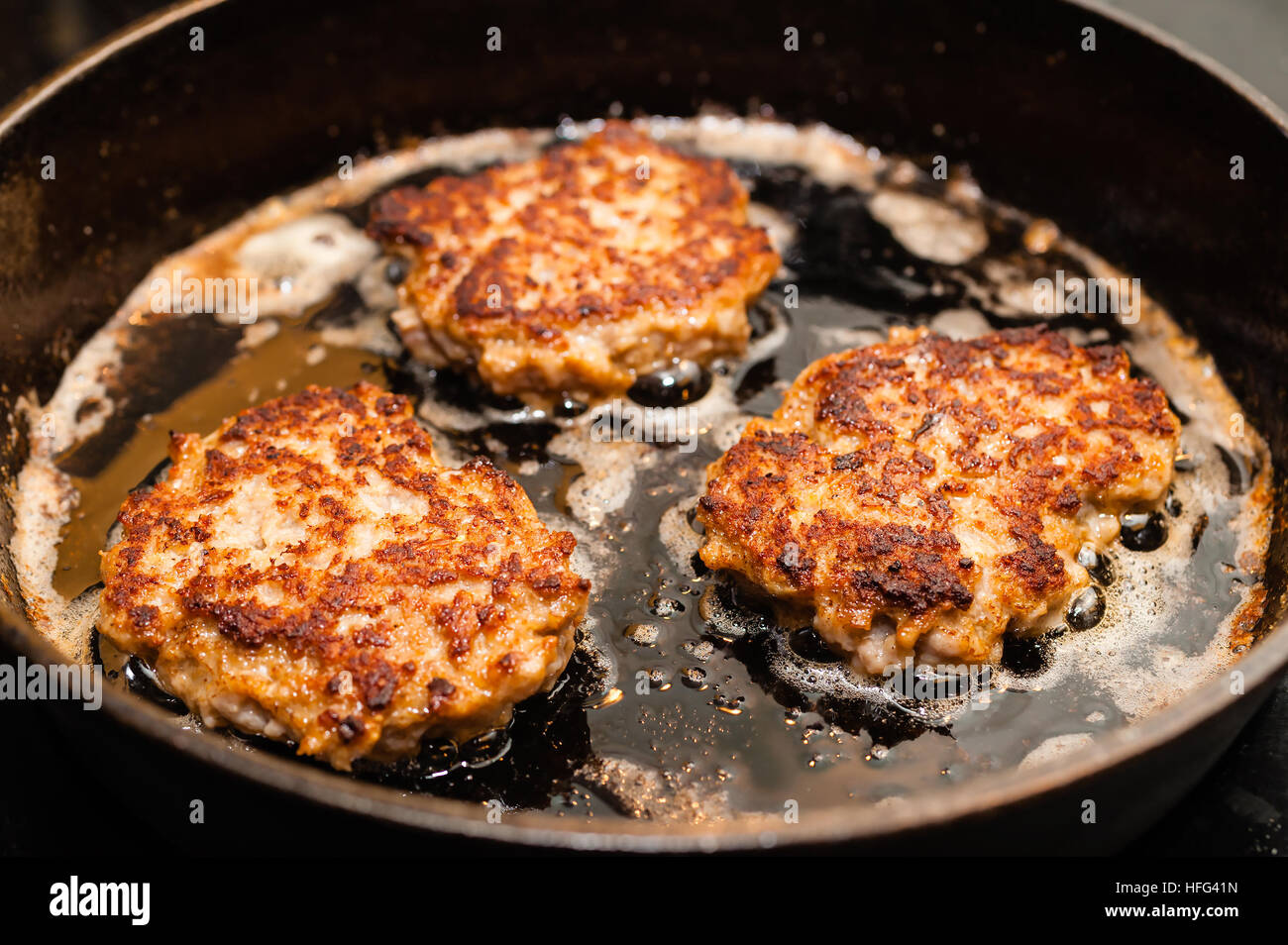Golden brown meat patties on hot cast iron skillet. Hot butter form