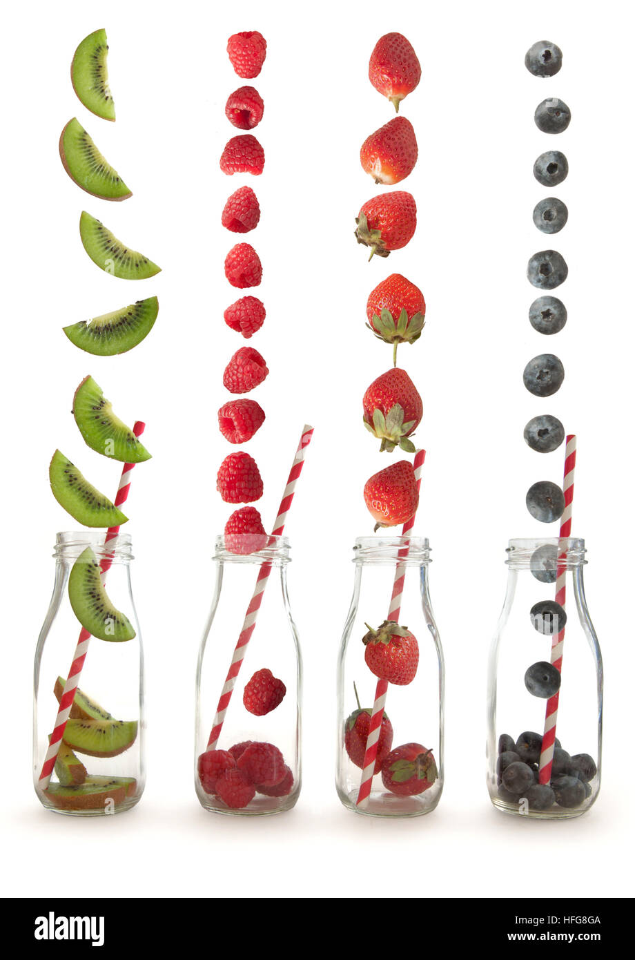 Berry fruits and kiwi falling into glass bottles with straws over a white background Stock Photo