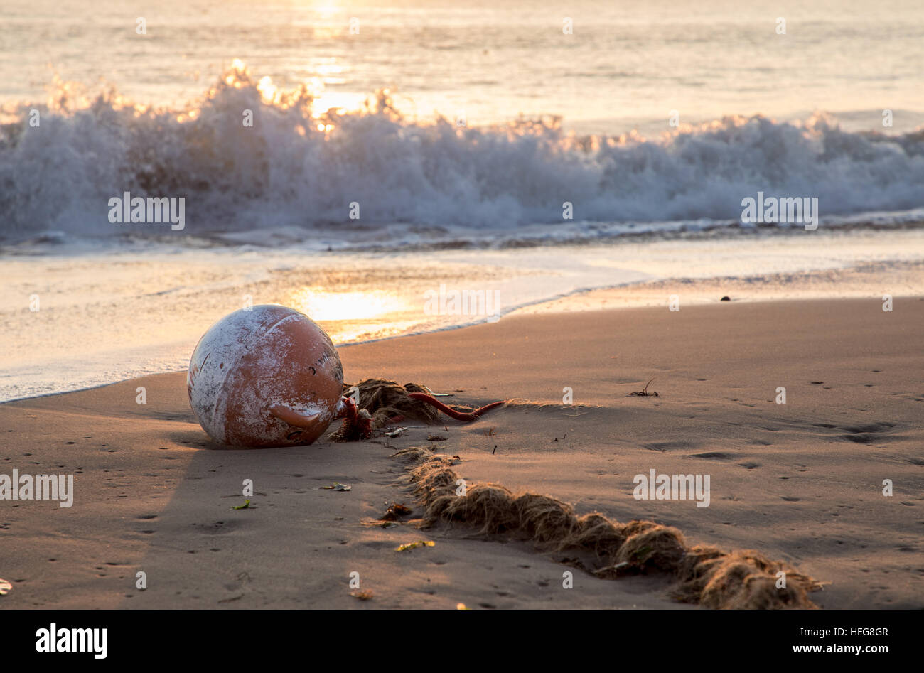 buoy and old worn rope beached in bay at sunrise Stock Photo