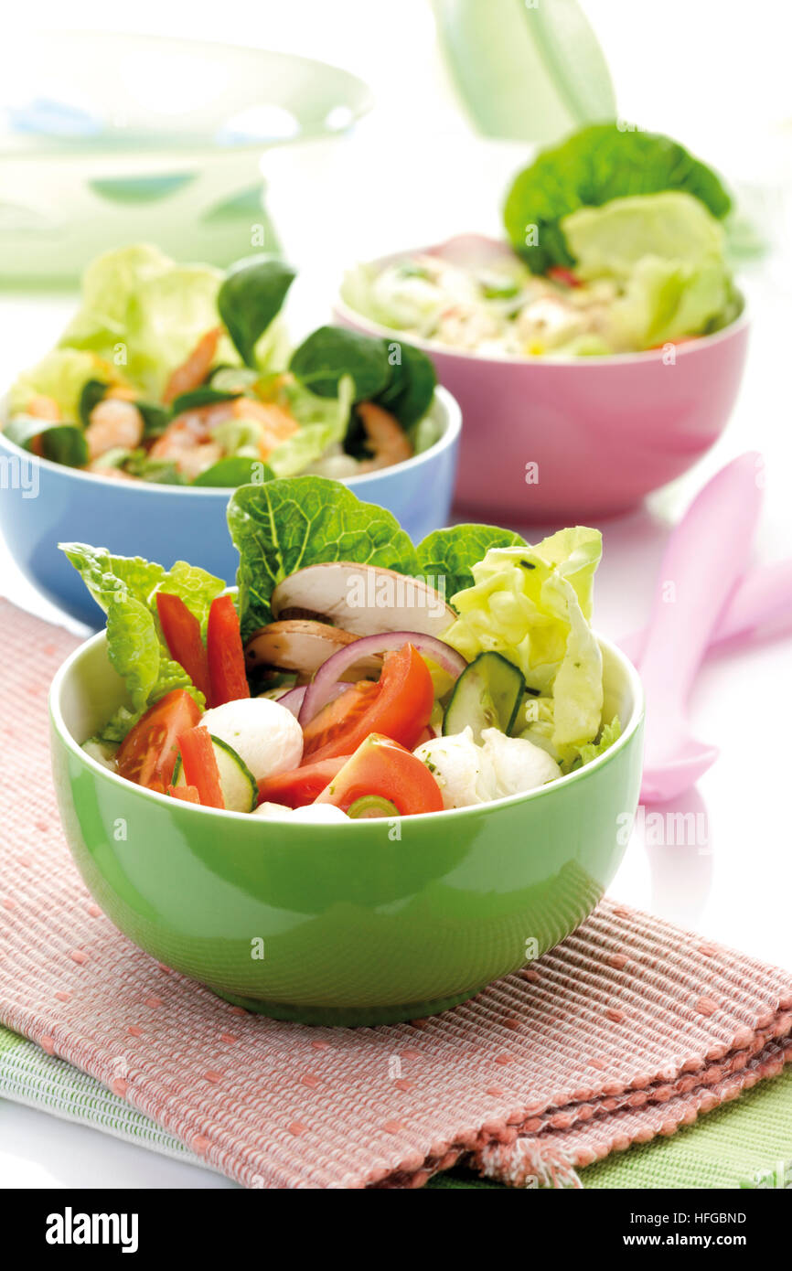 Salad in a bowl: romaine lettuce, cucumber, peppers, button mushrooms and mozzarella, various mixed salads in background Stock Photo