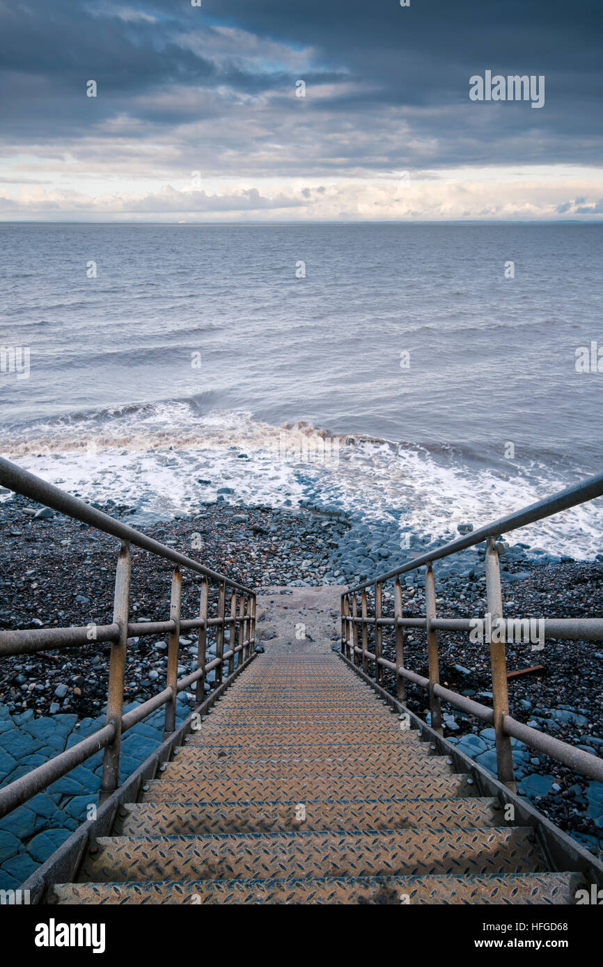 Metal stairway leading down to the incoming tide Stock Photo