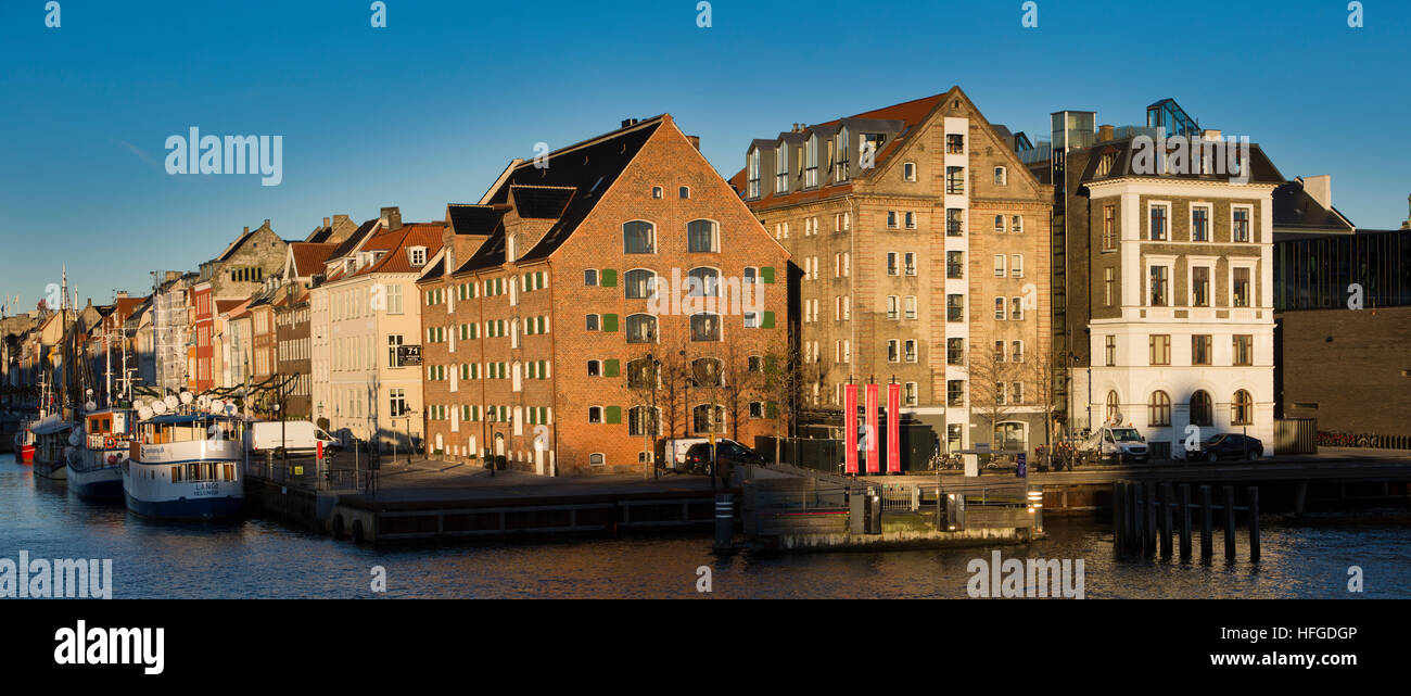 Denmark, Copenhagen, Nyhavn, boats moored beside quayside warehouses converted to hotels, housing and restaurants, panoramic Stock Photo