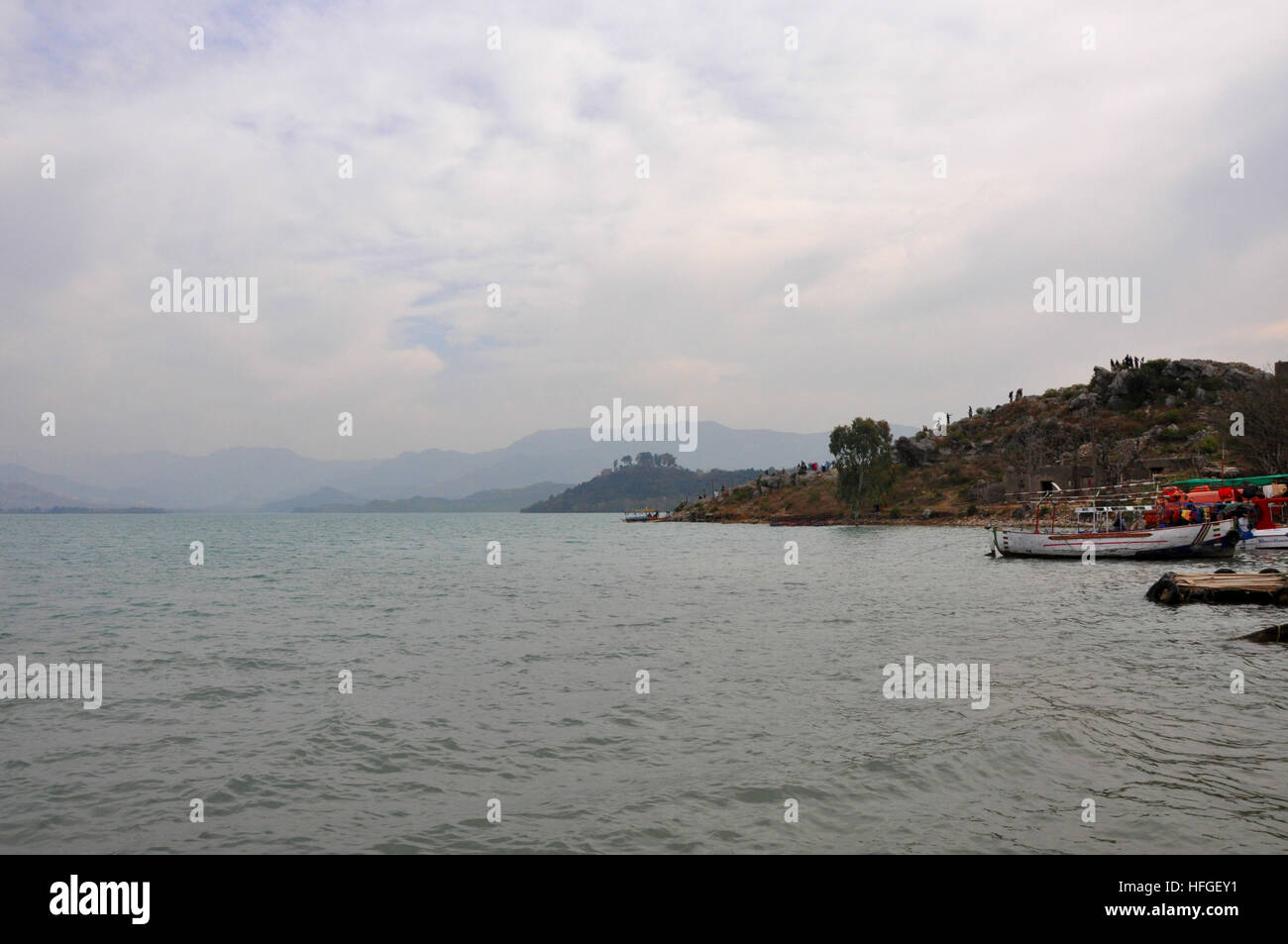 Boats on docks at Khanpur dam, Pakistan with clouds and distant mountain range in the background Stock Photo