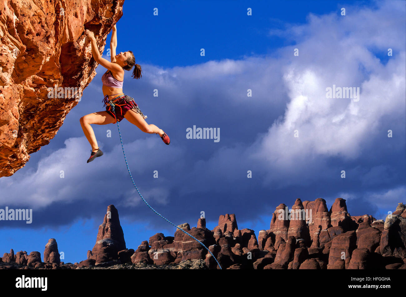 Female climber dangeling from the edge of a sheer rock mountain Stock