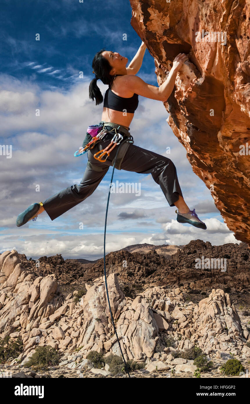 female asian rock climber dangles from the edge of a challenging cliff