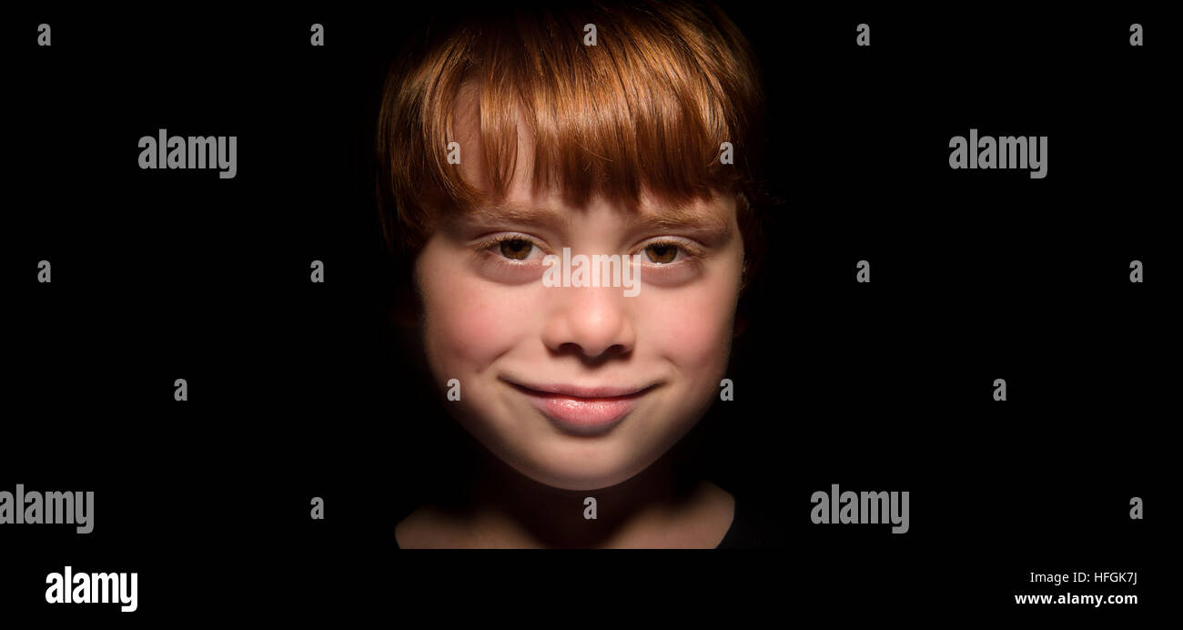 Low key portrait of ginger haired boy with black background Stock Photo