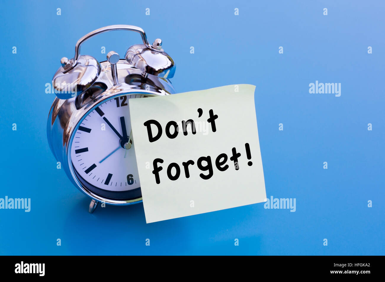 Dont Forget written on sticker with alarm clock on blue table Stock Photo