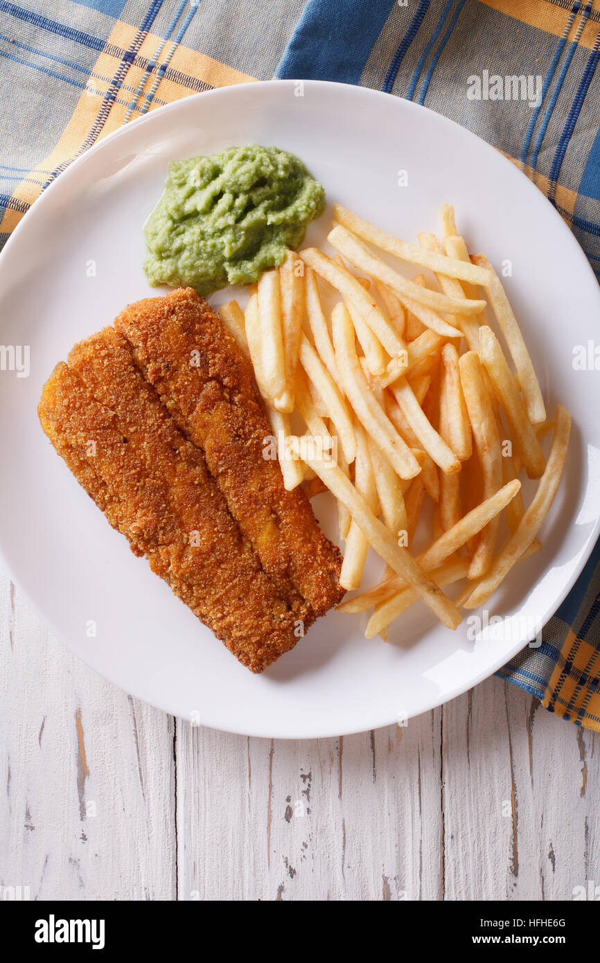 English food: fried fish in batter with chips and pea puree close-up on a plate. vertical top view Stock Photo