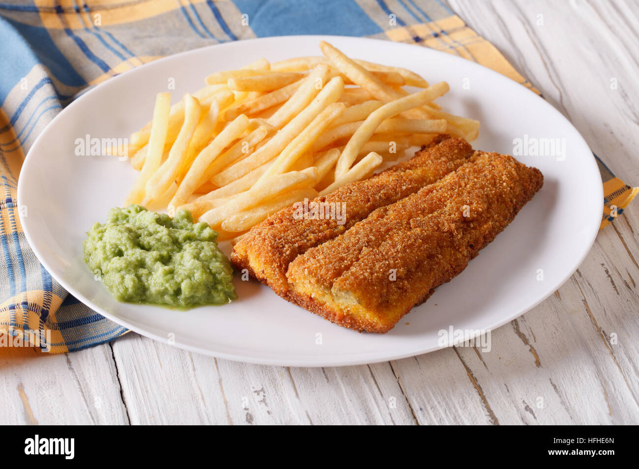 English food: fish in breadcrumbs with fried potatoes and pea puree on a plate. horizontal Stock Photo