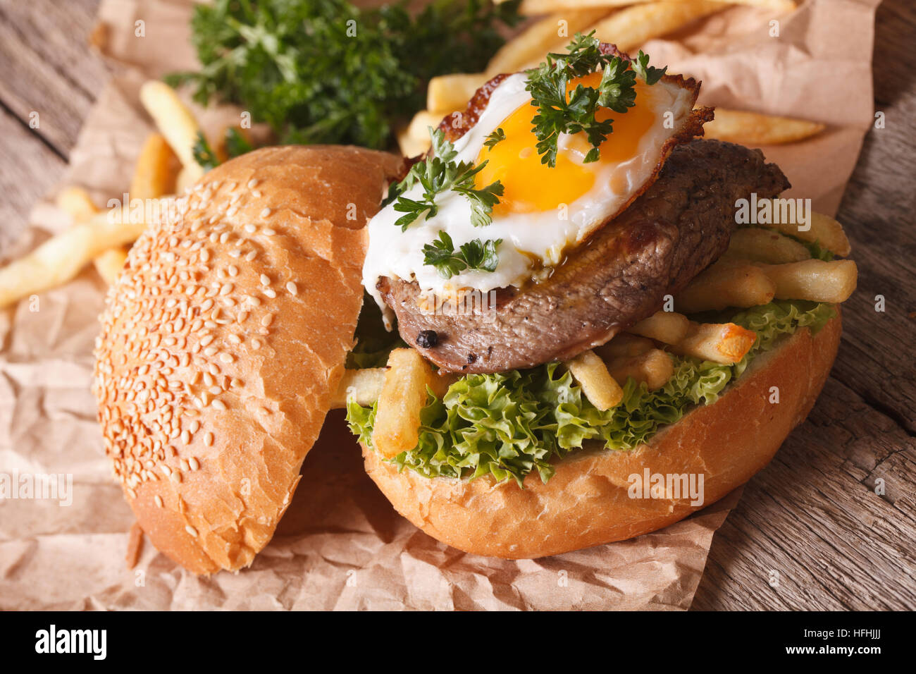Sandwich with beefsteak, fried egg and French fries close-up. Horizontal Stock Photo
