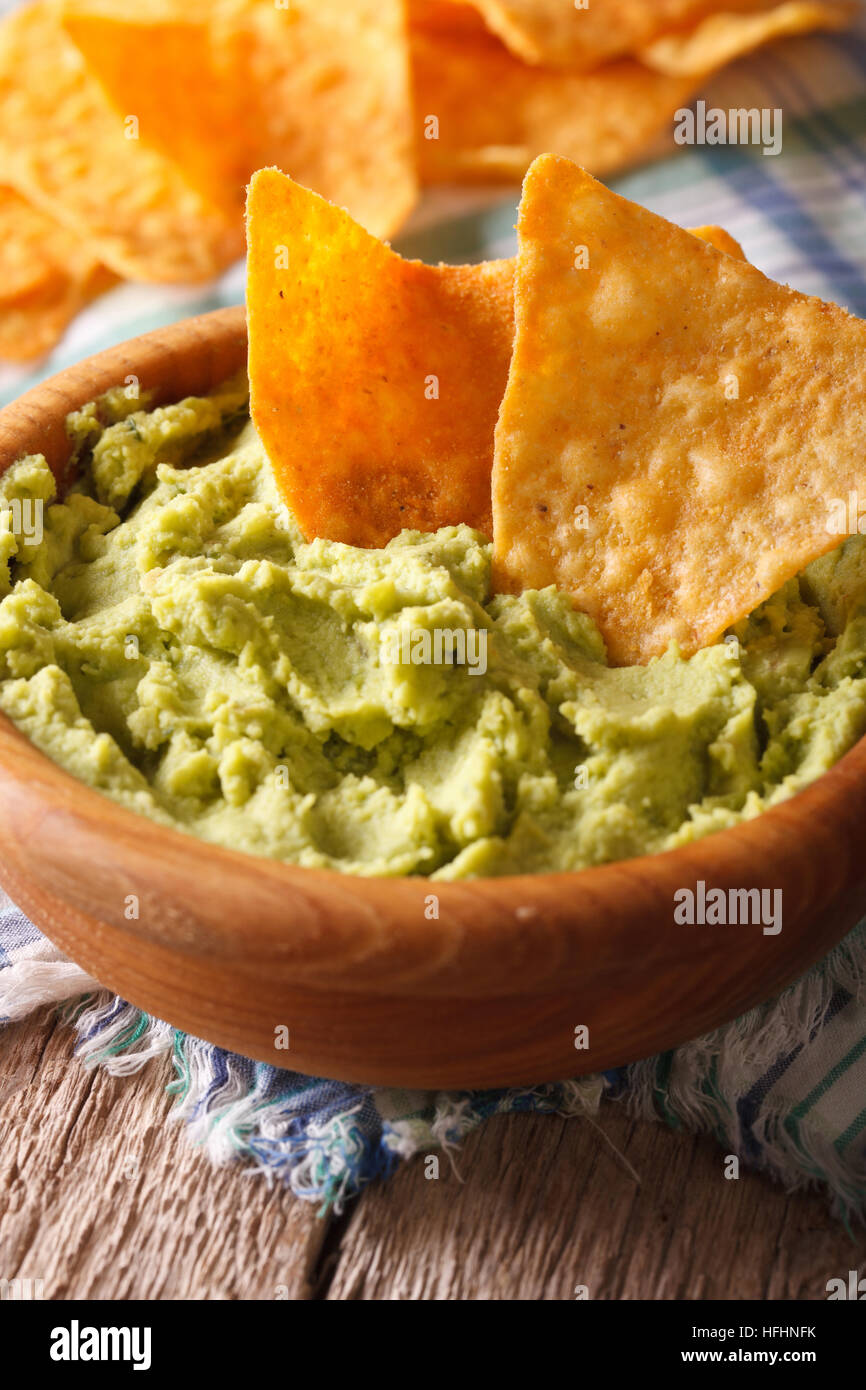 guacamole and nachos chips macro in a wooden bowl. Vertical, rustic style Stock Photo