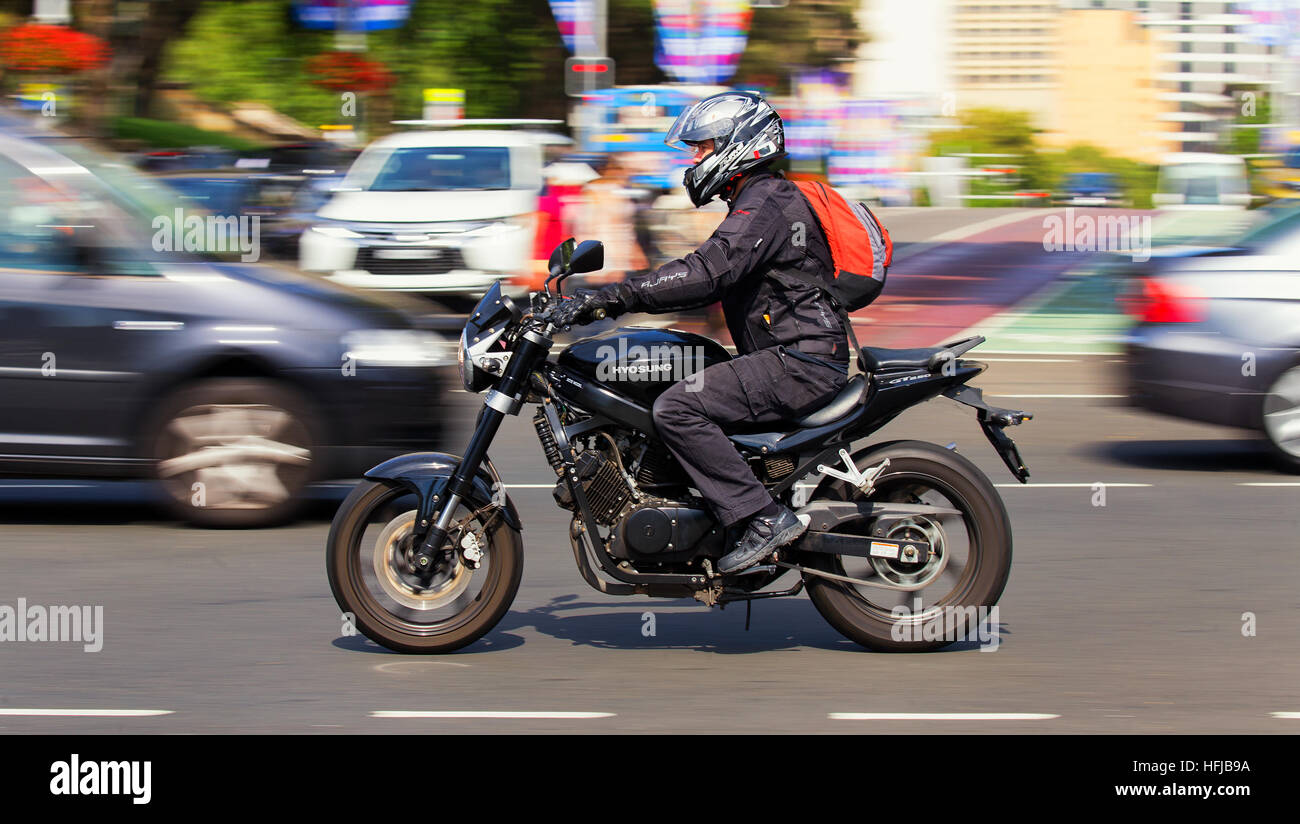 A man commutes across the city centre on a motorbike in the morning rush hour. Panning has blurred the background Stock Photo