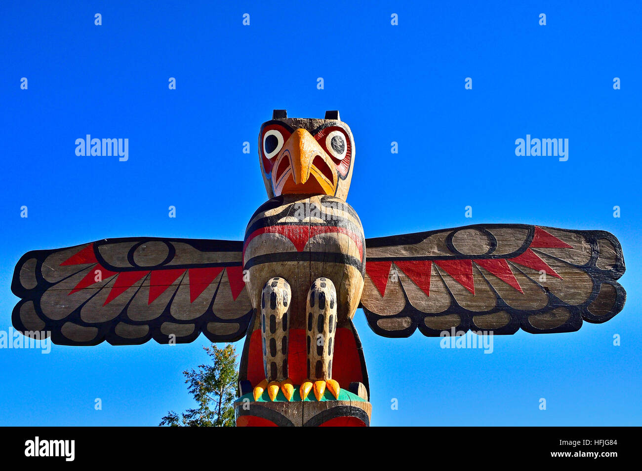 A native bird carving at the top of a totem pole Stock Photo