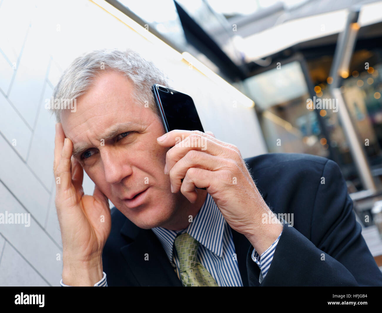 Worried businessman, bad news, looking concerned listening intently on his smartphone iPhone 7 plus mobile telephone at alfresco restaurant bar table Stock Photo