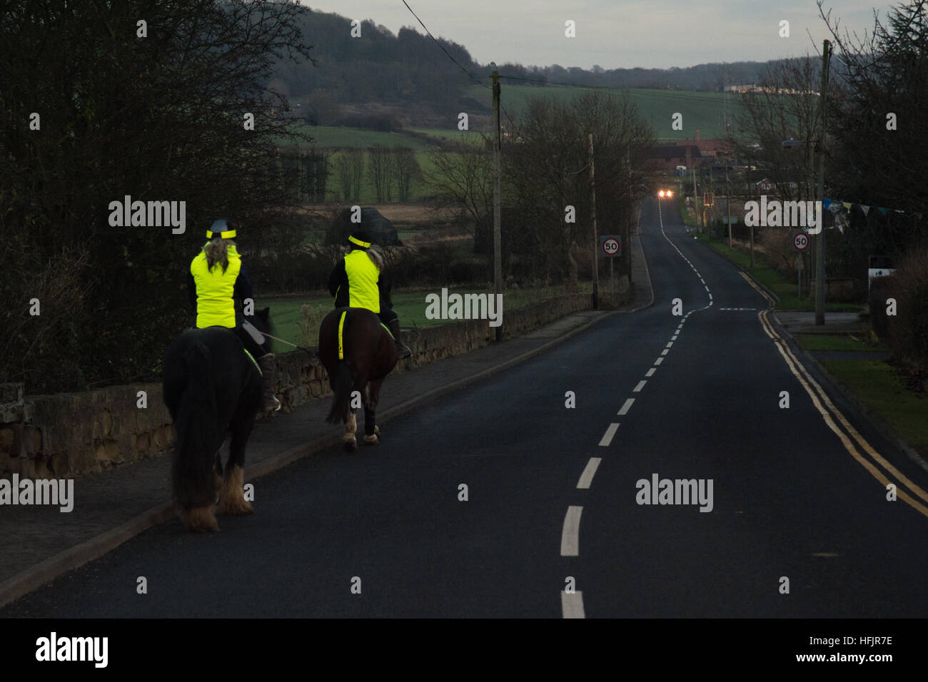 Two female horse riders wearing high visibilty clothing on dark rural road Stock Photo